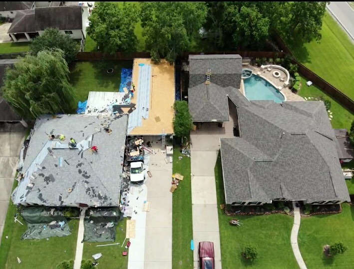 Aerial view of a roof tear-off with debris on tarps, pool visible in yard