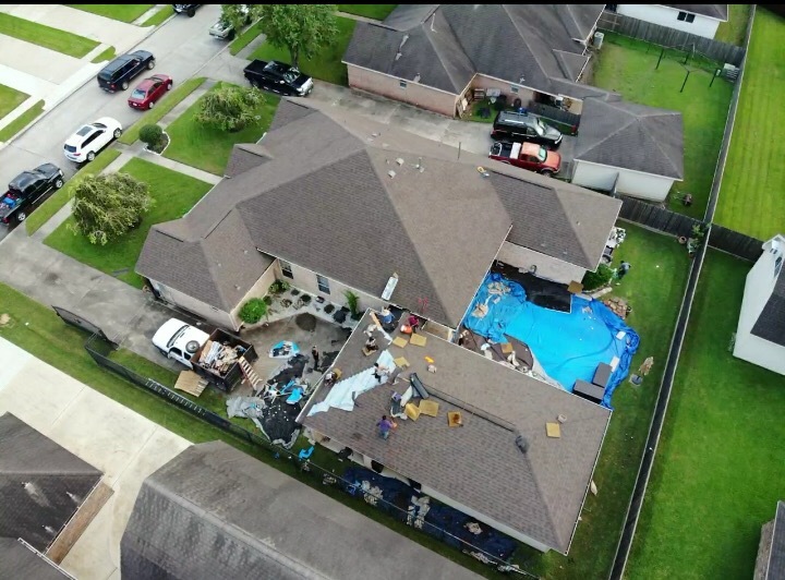 Aerial view of a home during a roof tear-off with pool covered for protection