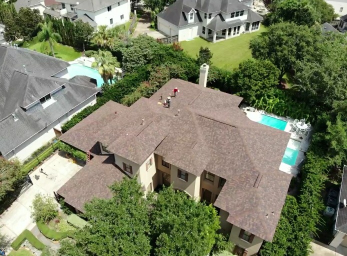 Crew finishing a completed brown shingle roof near a backyard pool
