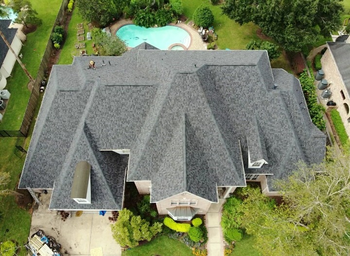 Completed gray shingle roof on a two-story home with pool and landscaping